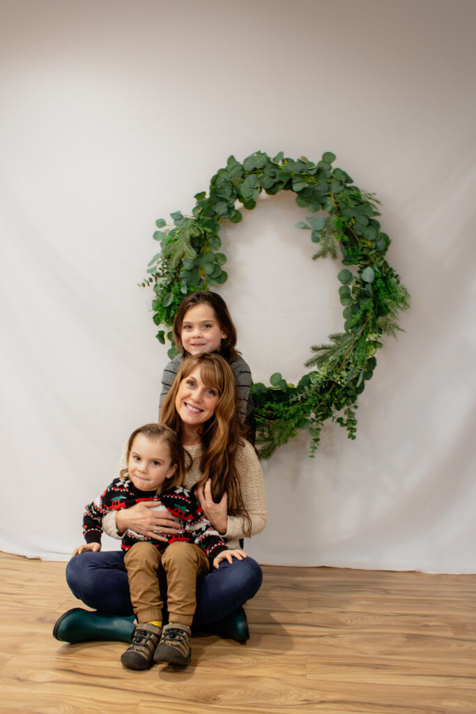 Mom and sons pose in front of wreath for Christmas Mini photography session in Roseburg Oregon by McKenzie Strong Photography.