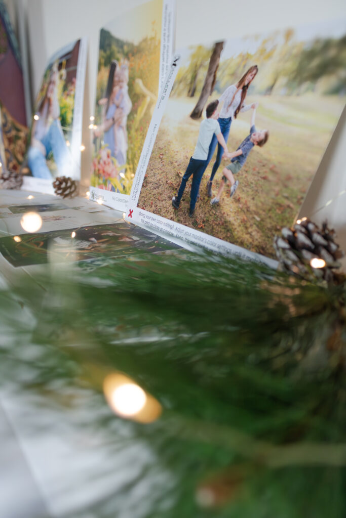 Close-up of printed family photos displayed with pine greenery and twinkle lights inside a photography studio.