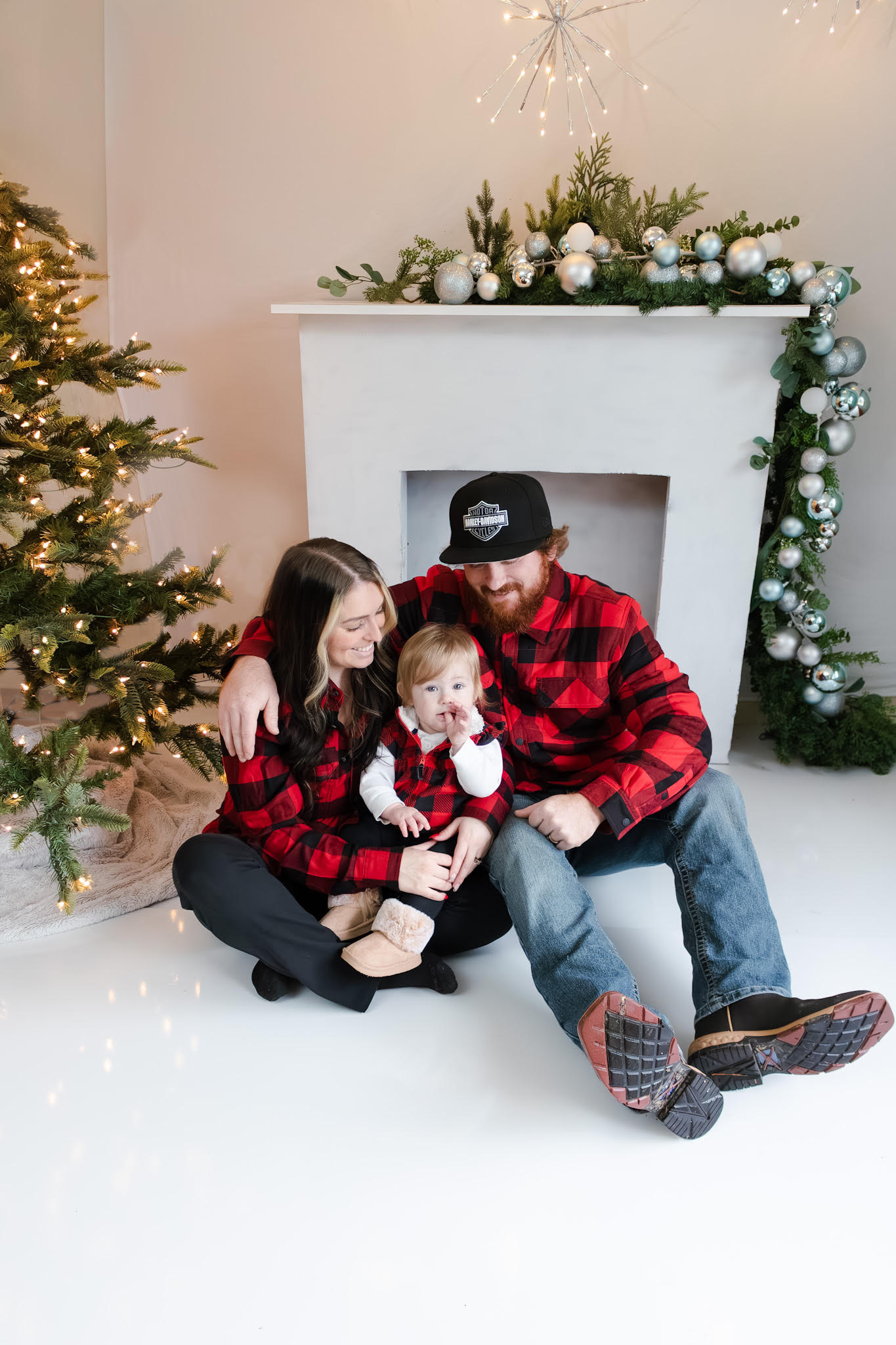 Family in matching red plaid outfits during Christmas mini session in Roseburg Oregon studio with decorated tree and fireplace