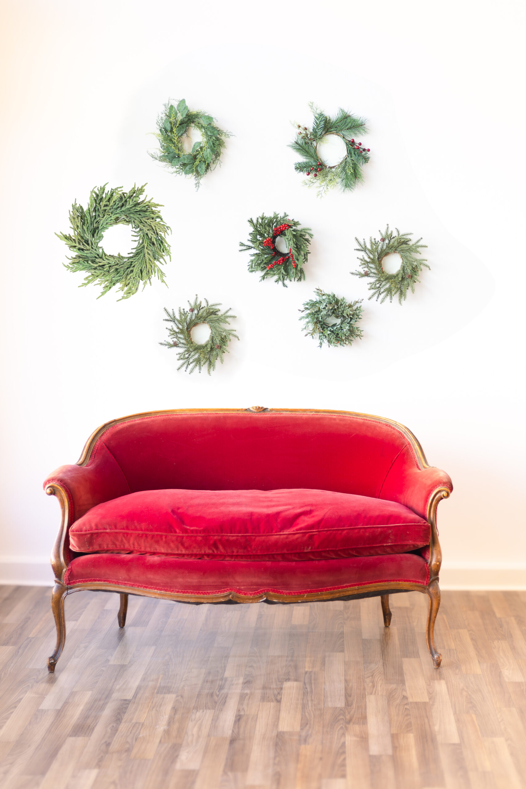 Antique red velvet couch in front of a wall of wreaths for indoor Roseburg Christmas minis with McKenzie Strong Photography.
