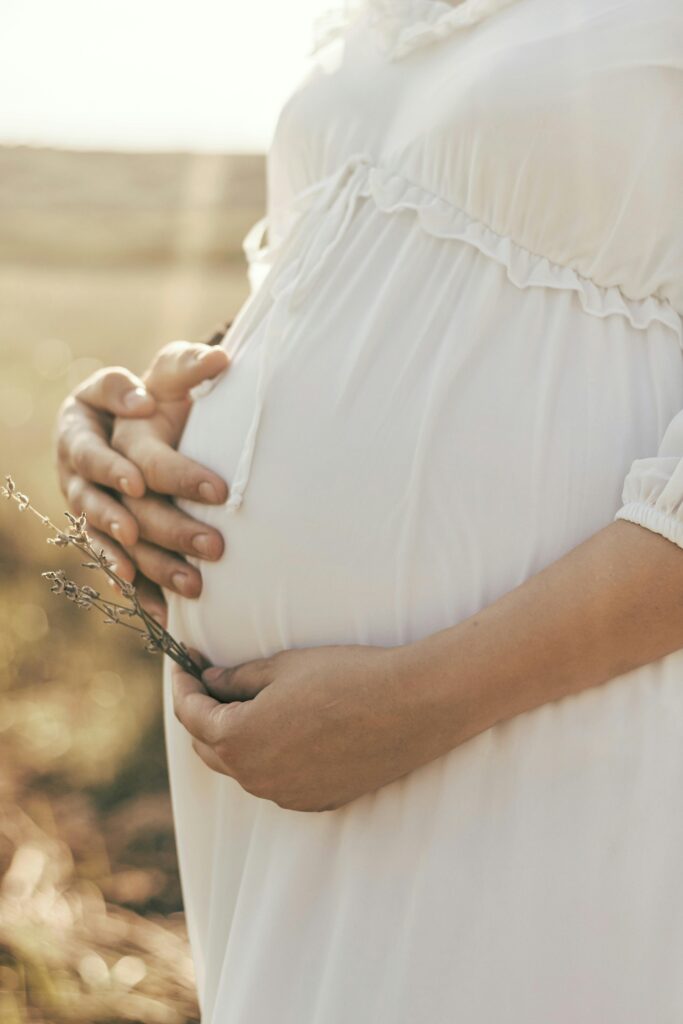 Maternity portrait in Roseburg, Oregon with expecting mother in white dress holding her belly at Discovery Garden.